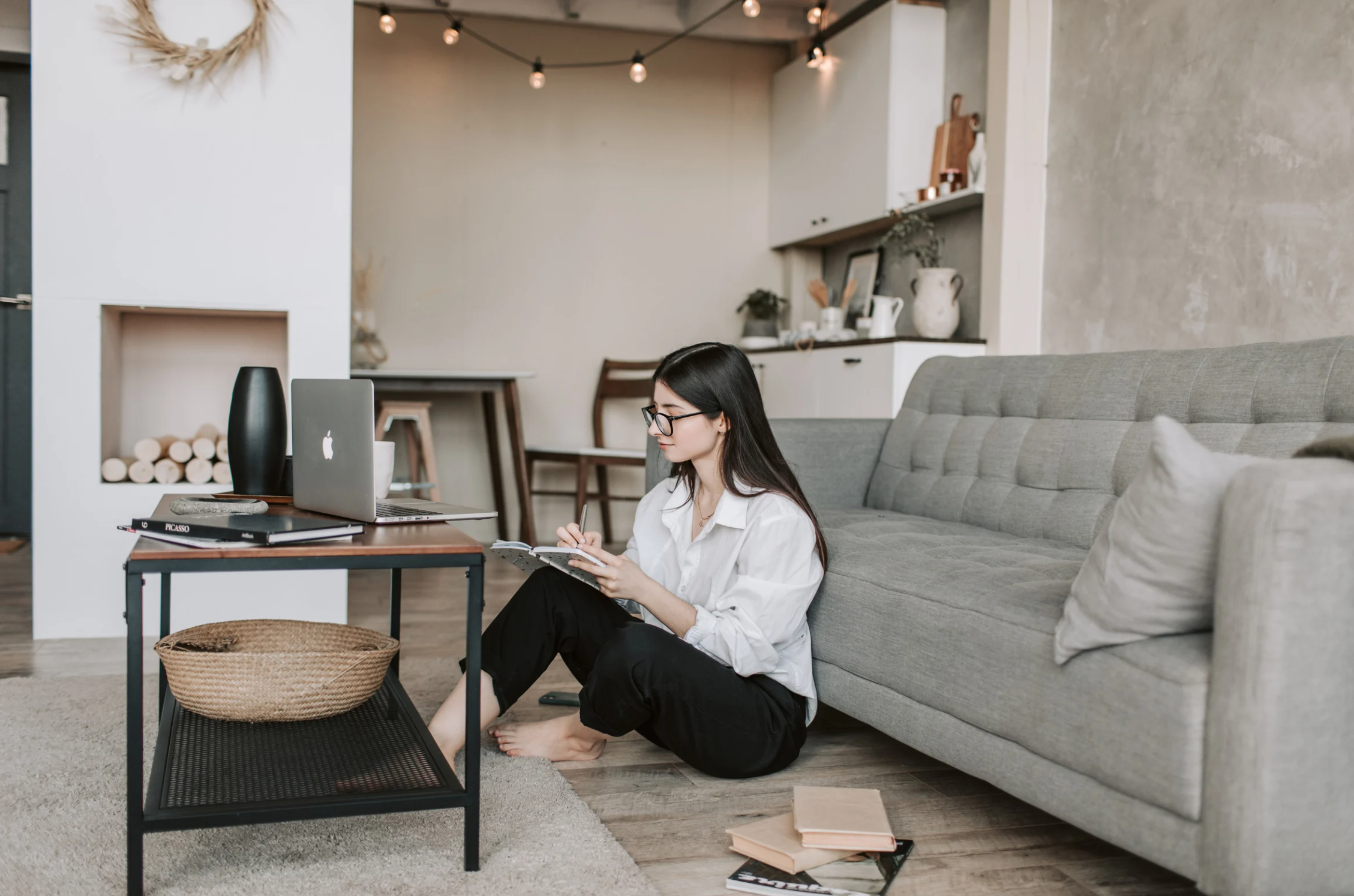 Female business owner sitting on floor looking at laptop and writing notes.